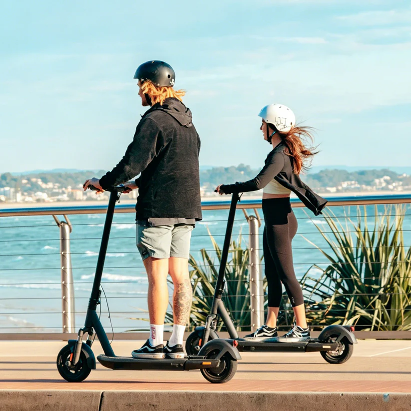 Two people riding electric scooters along waterfront